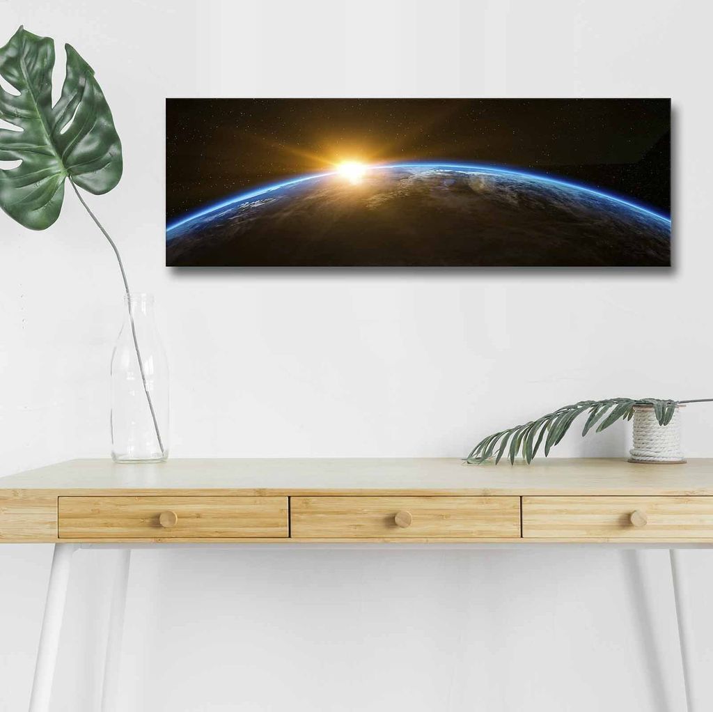 A panoramic canvas print of Earth at sunrise is displayed on a white wall above a wooden desk.