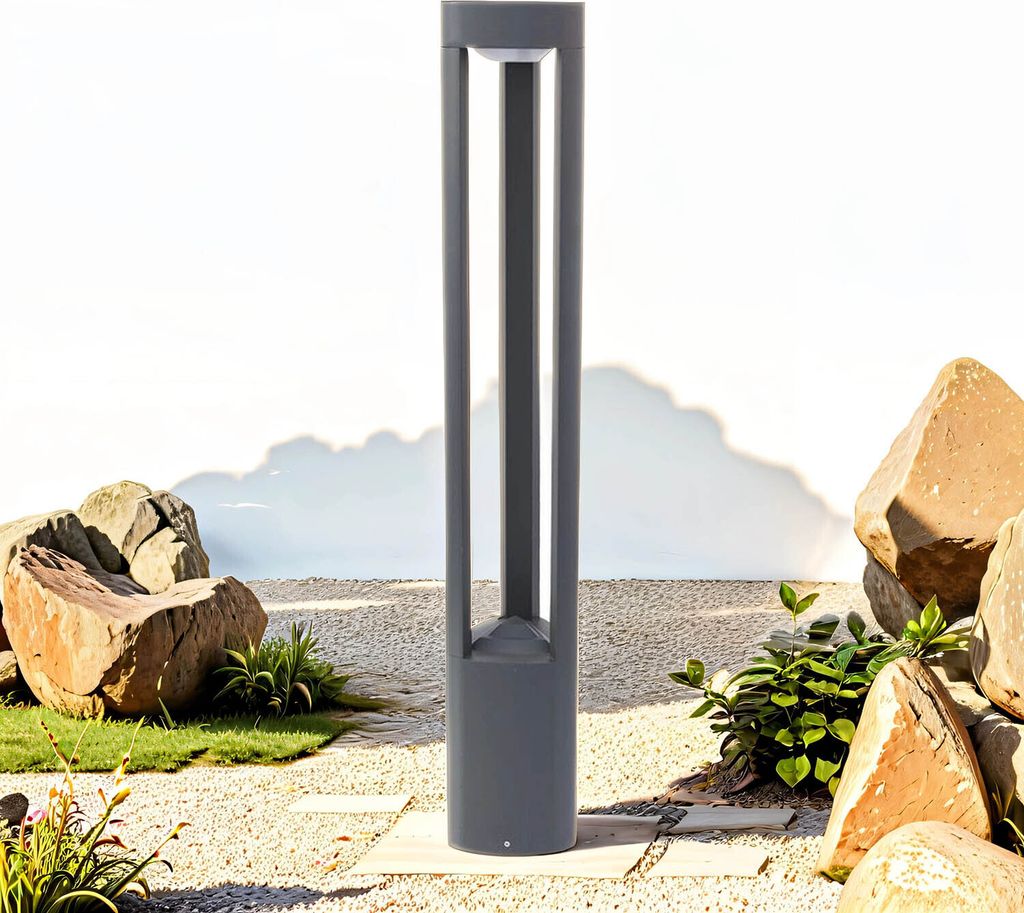 A modern gray outdoor lamp stands in a garden setting with rocks and gravel.