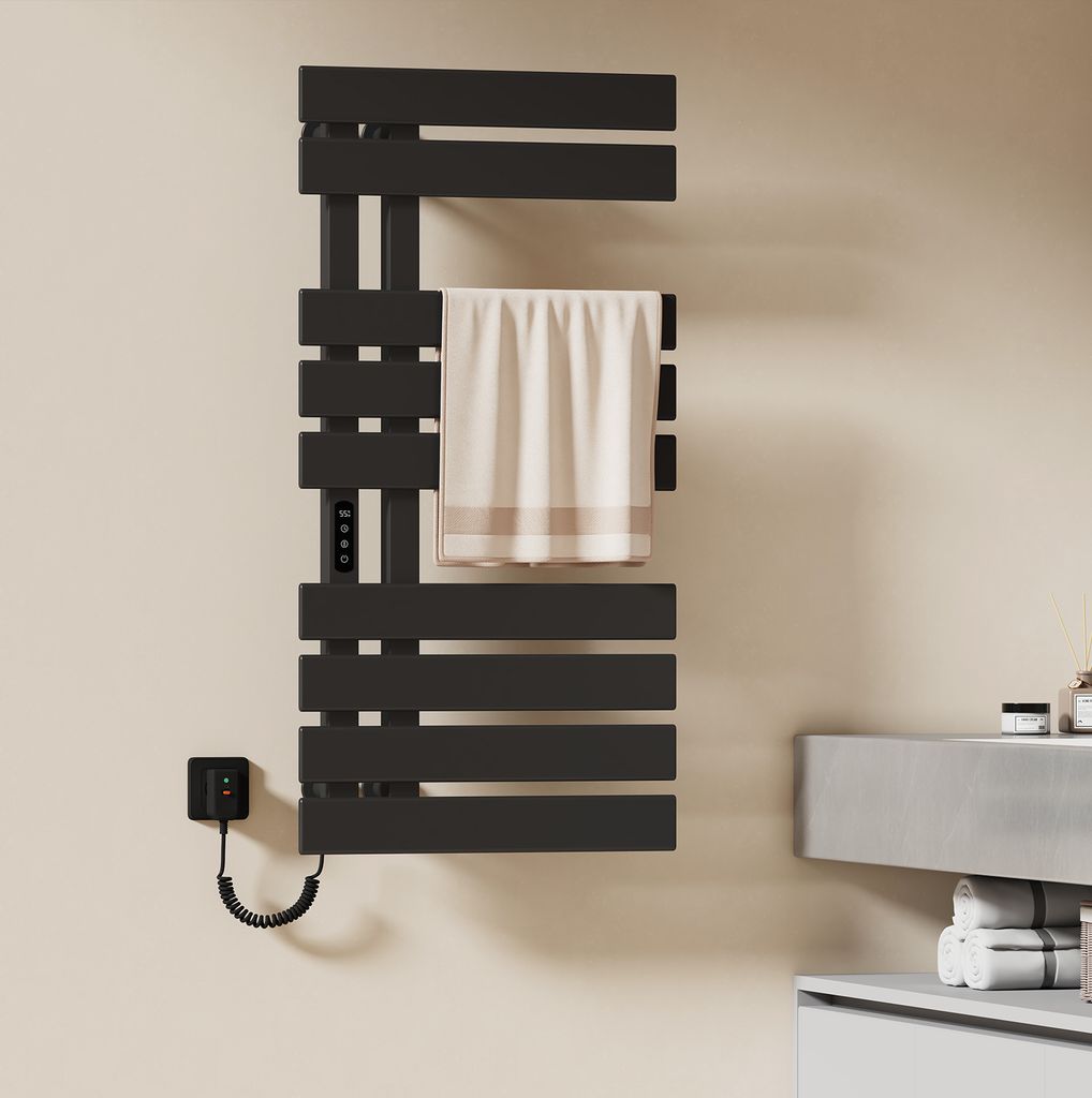 A black electric towel warmer mounted on a light beige wall, with a towel draped over one of its bars. A small black control unit is attached to the wall to the left of the warmer.
