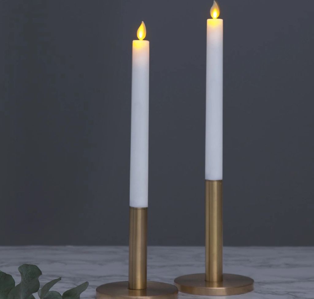 Two LED candles in gold candle holders against a dark gray background.