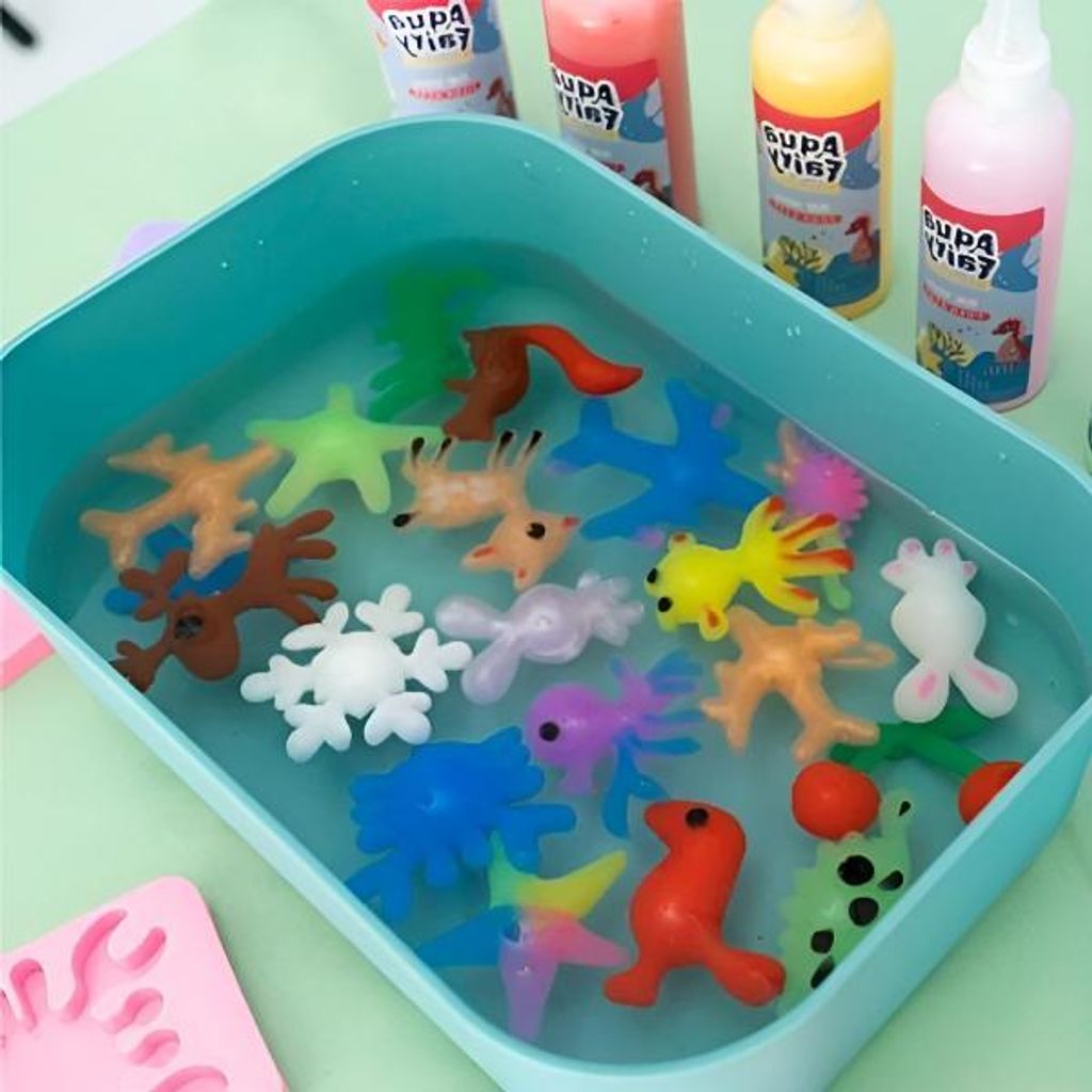 Sortiment aus bunten Plastik-Tier- und Schneeflocken-Spielzeugen, die in einer hellblauen Wanne im Wasser schwimmen