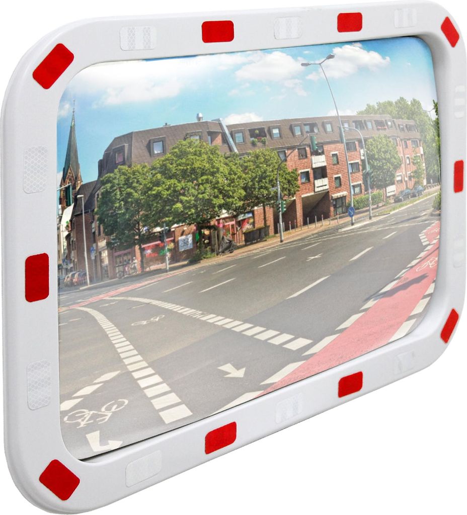 A convex mirror with a white frame and red reflectors, reflecting a street scene with buildings and a road.