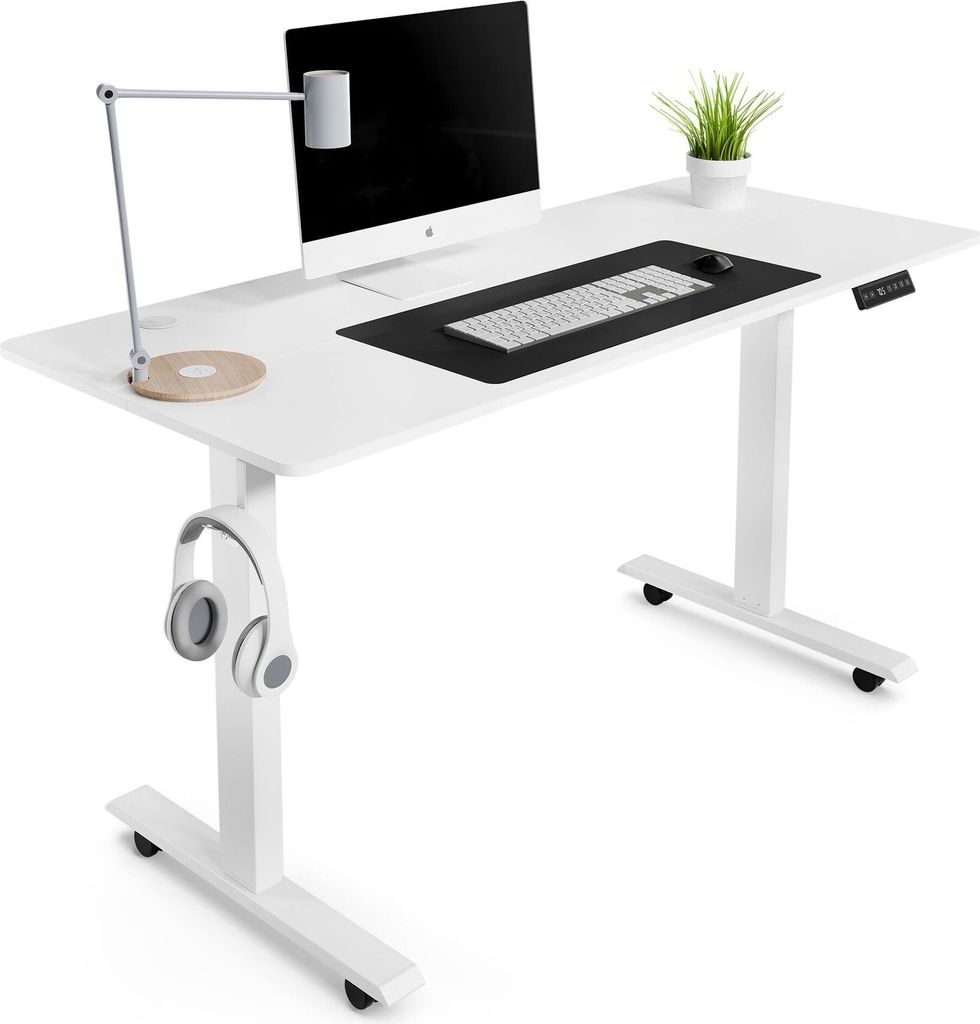 A white adjustable standing desk with a computer, keyboard, mouse, lamp, and headphones.