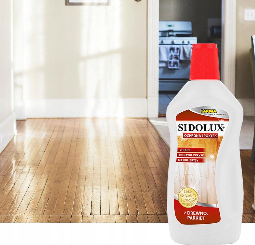 A bottle of wood polish is placed in front of a wooden floor in a hallway, with a kitchen visible in the background.
