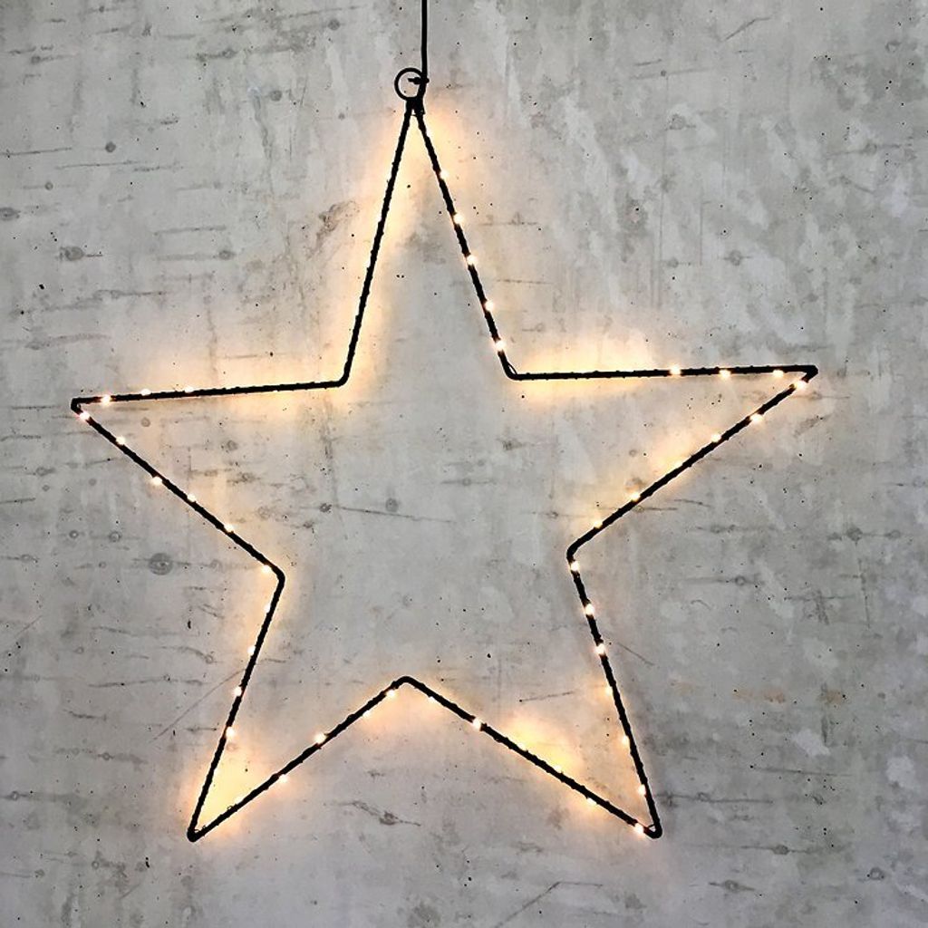 A black wire star outline with warm white LED lights is hanging against a textured gray wall.
