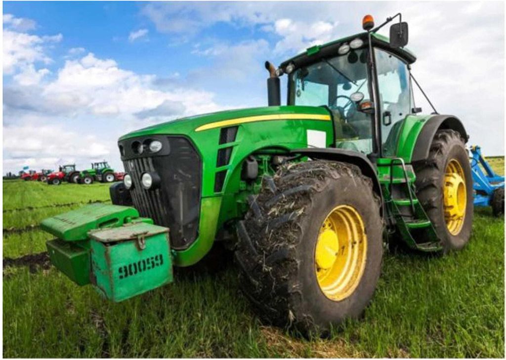 A green tractor is parked in a grassy field under a blue sky with white clouds. Other tractors are visible in the background.