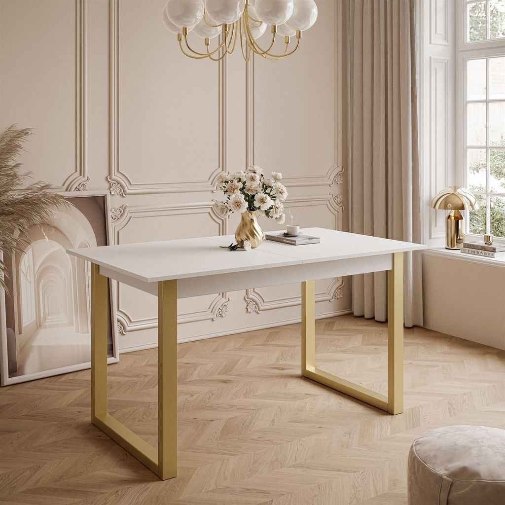 A white dining table with gold legs is shown in a room with decorative wall molding and a large window with curtains.