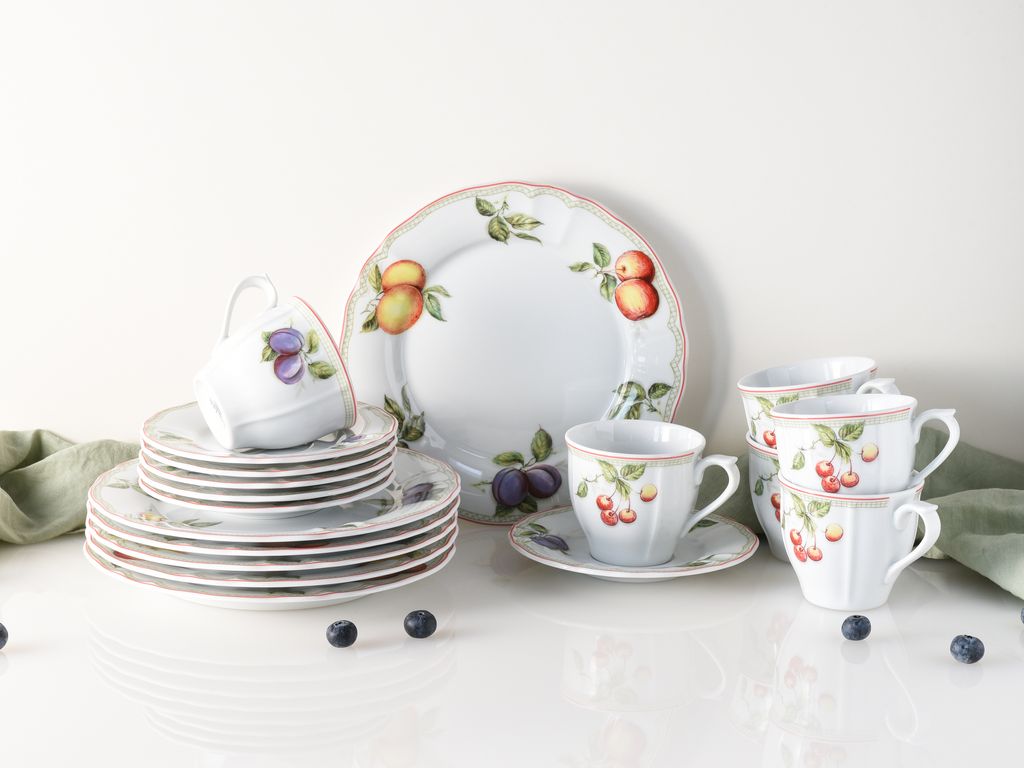 A set of porcelain dishes with fruit illustrations, including plates, cups, and saucers, arranged on a white surface.