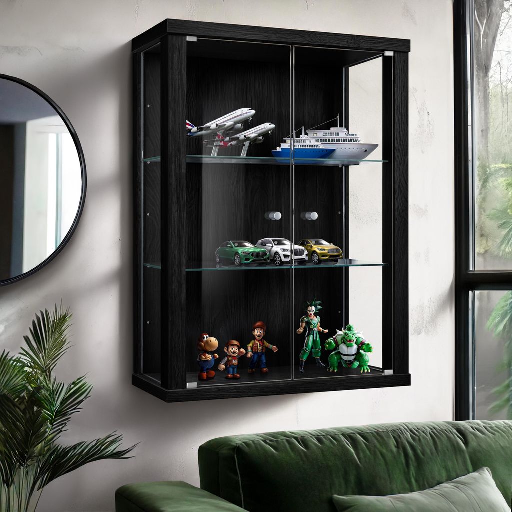 A black wall-mounted display cabinet filled with various collectible models, including airplanes, cars, and figurines, is shown in a room setting with a green sofa and a round mirror on the wall.