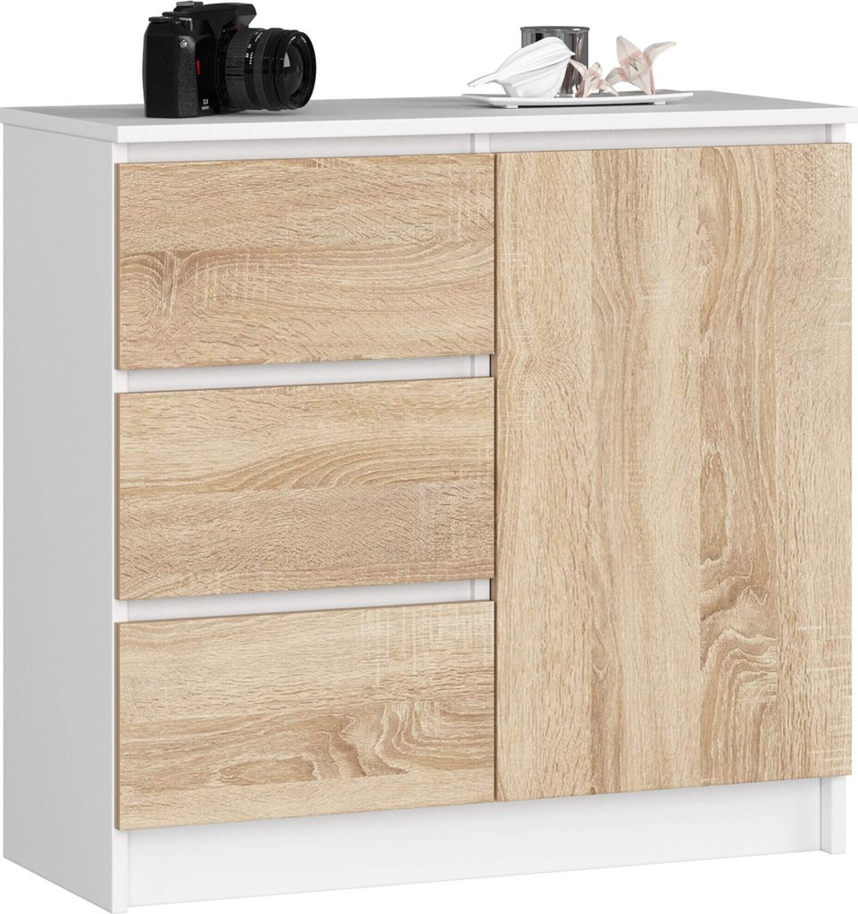 A white and wood cabinet with three drawers and a cabinet door, on a white background. A camera and some decorative items are on top.