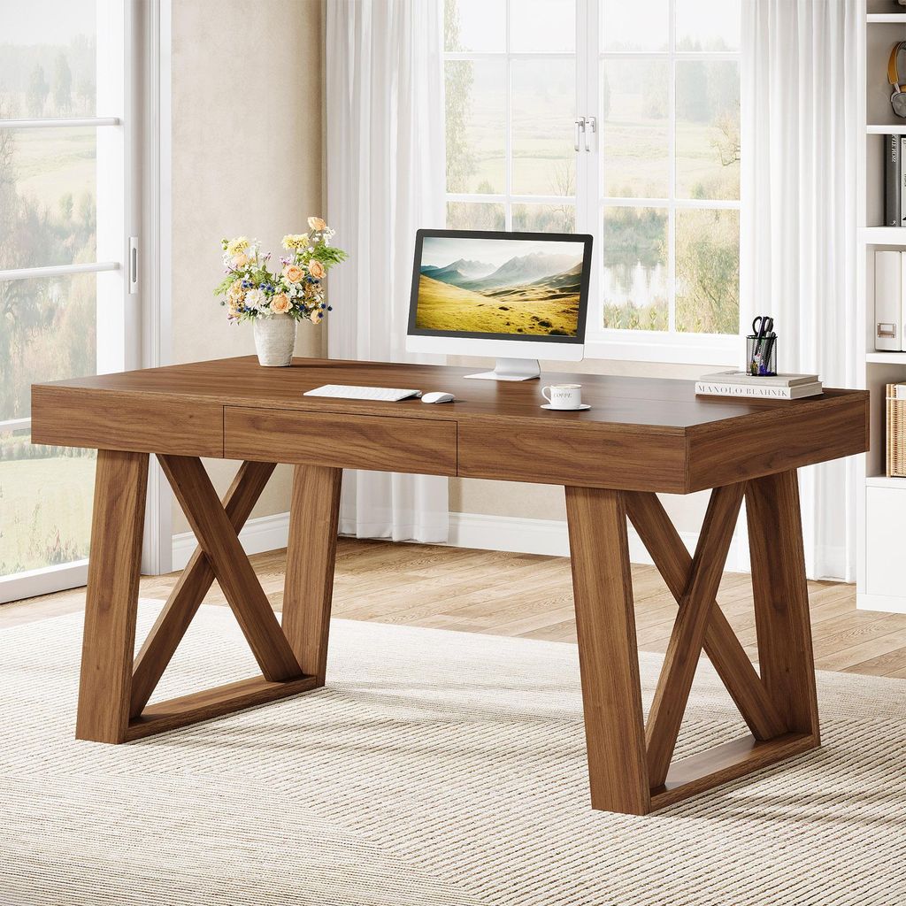 A wooden desk with a computer and flowers in a bright room.