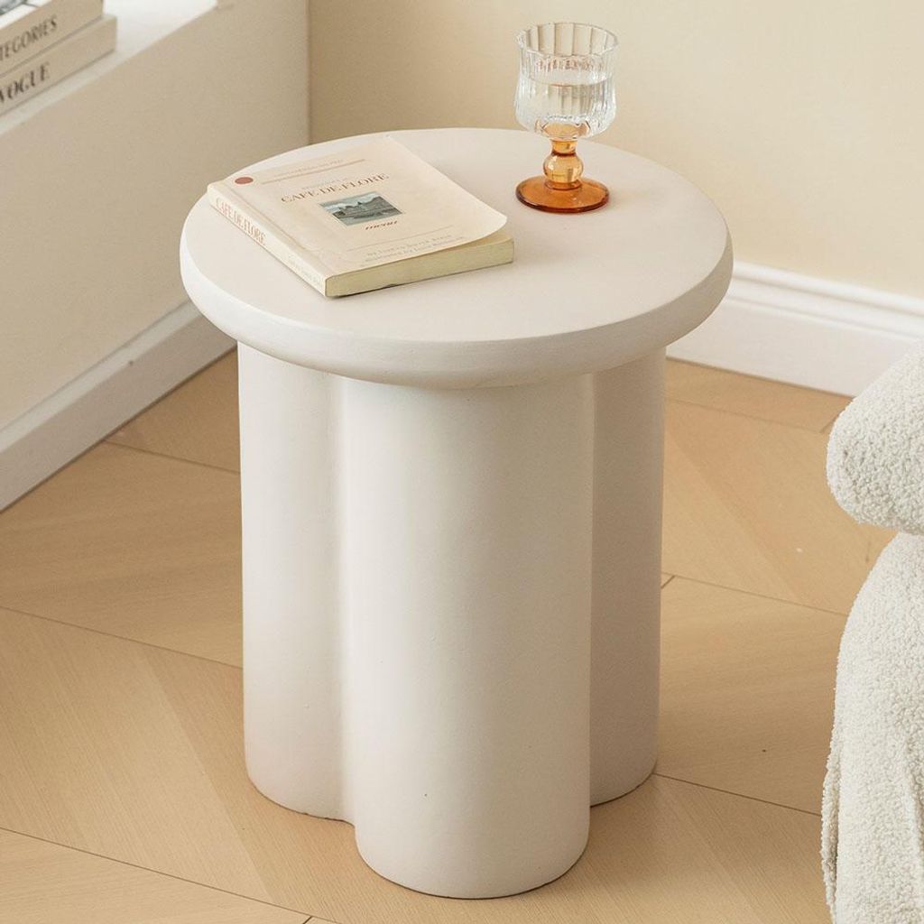 A white side table with a book and a glass of water on it, placed on a light wooden floor.