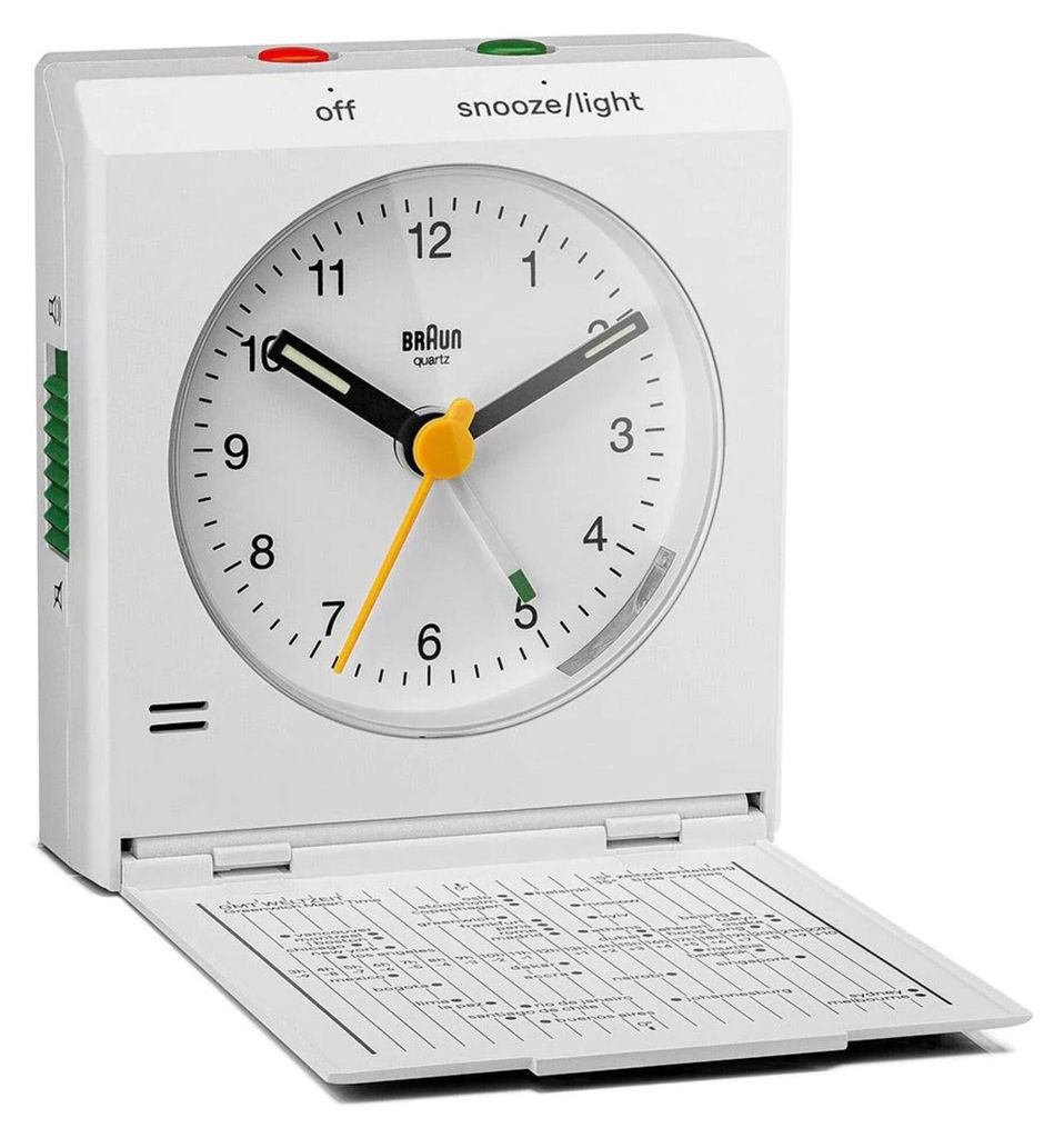 A white Braun alarm clock with its front cover open, revealing the clock face and a small information sheet underneath.