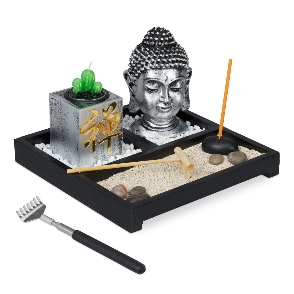 A Zen garden set with a Buddha head, a cactus candle, a rake, incense, and stones on a black tray.