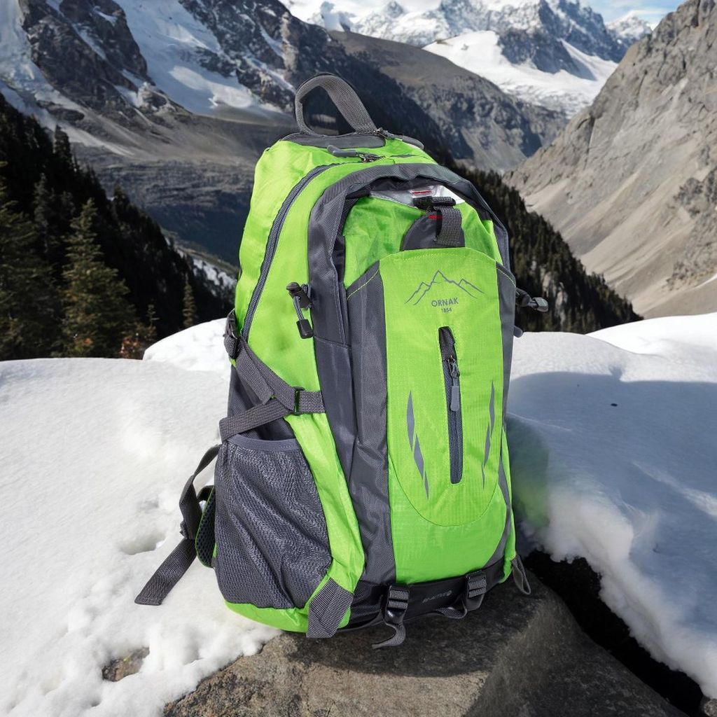 A green and gray backpack is placed on a rock in a snowy mountain landscape.