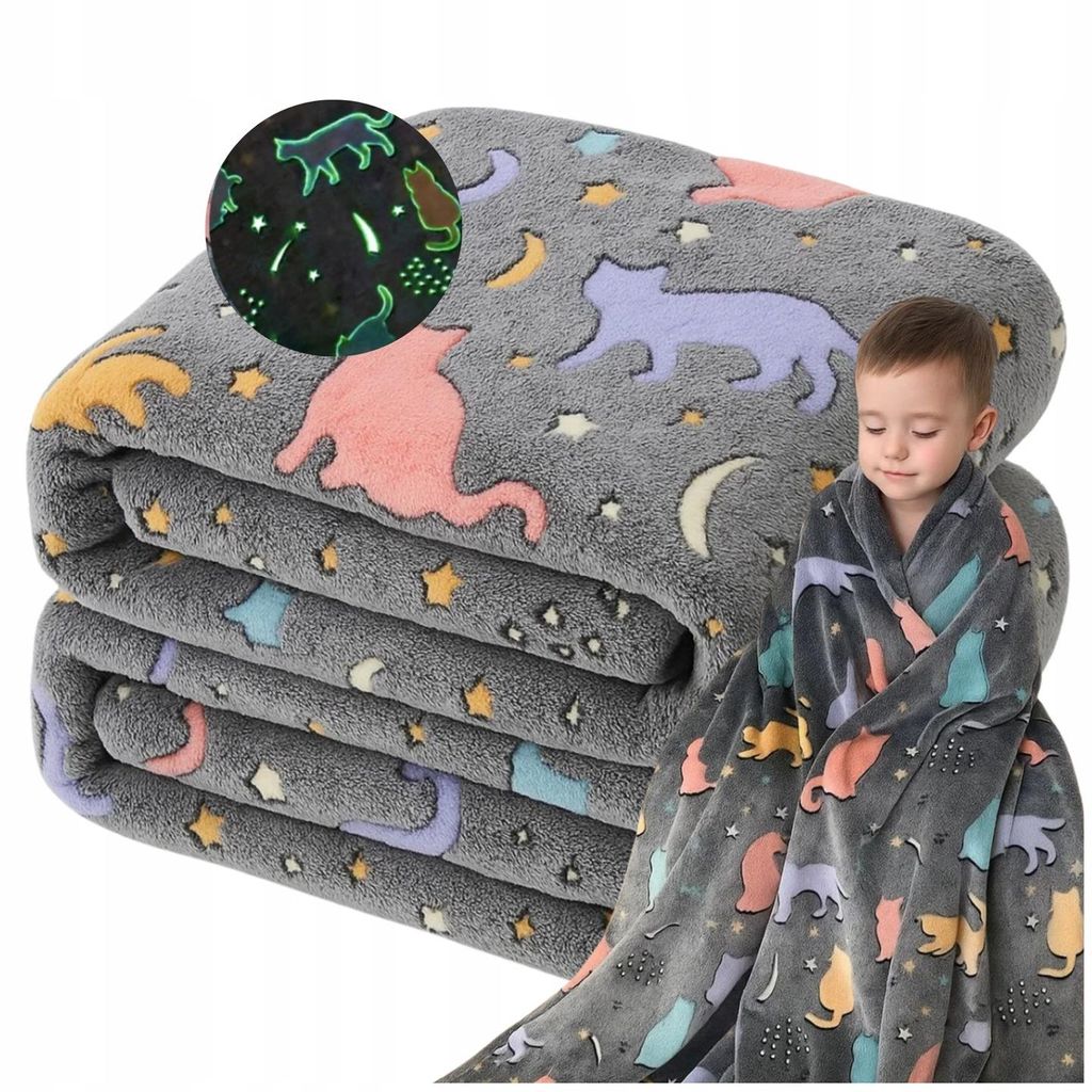 A child wrapped in a glow-in-the-dark cat-themed blanket, with a folded stack of the same blankets in the background.