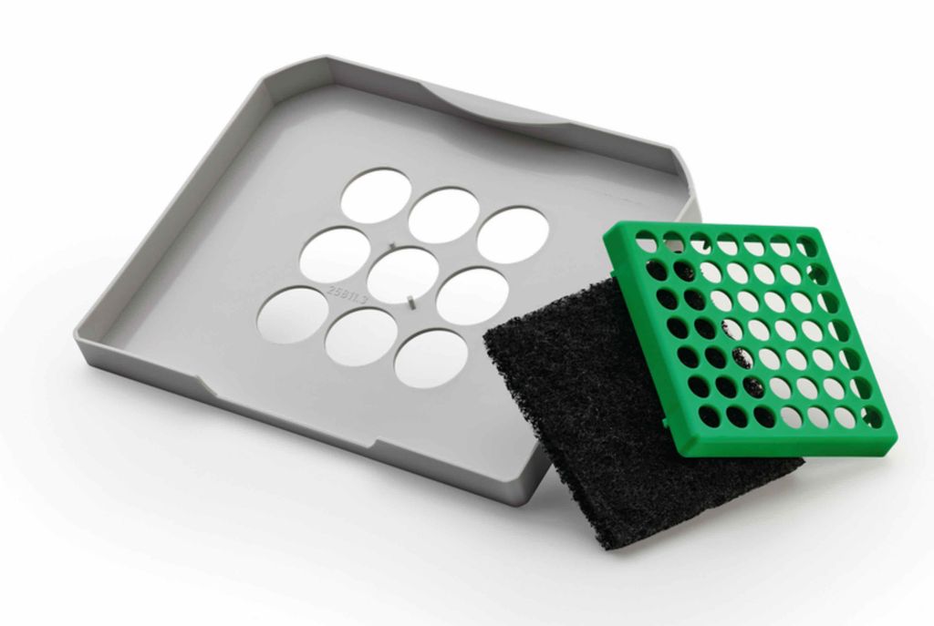 A gray tray with circular openings, a black filter, and a green grate are arranged on a white background.
