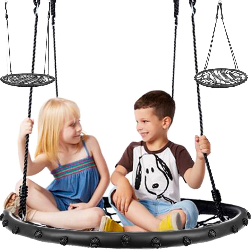Two children are sitting on a large, round swing, smiling and looking at each other.