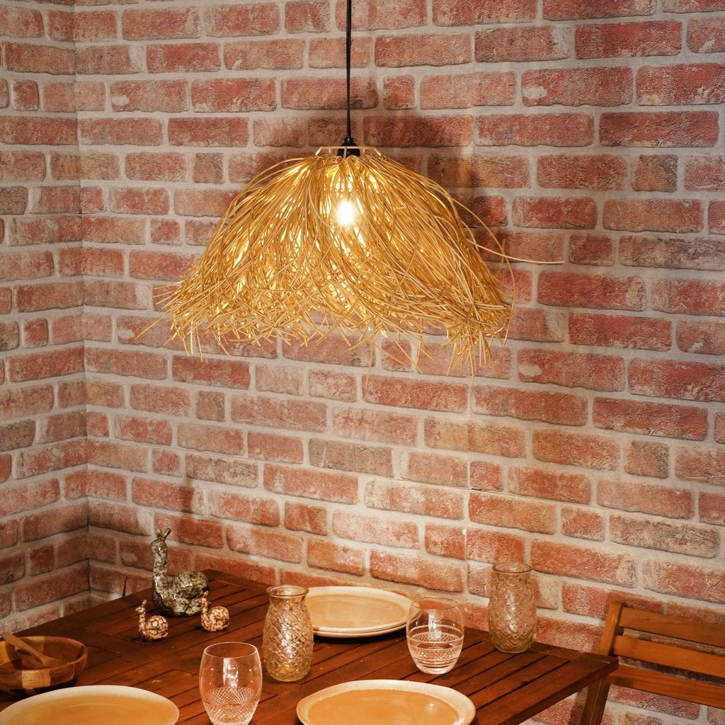 A hanging lamp made of straw-like material is illuminated above a wooden table set with plates and glasses.