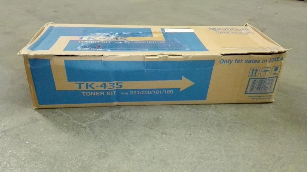 A cardboard box for a Kyocera toner kit sits on a concrete floor.