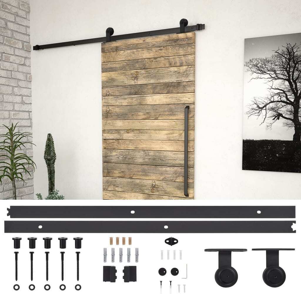 A sliding barn door with a black metal track and hardware, displayed against a white wall with a framed picture of a tree and a plant in a pot.
