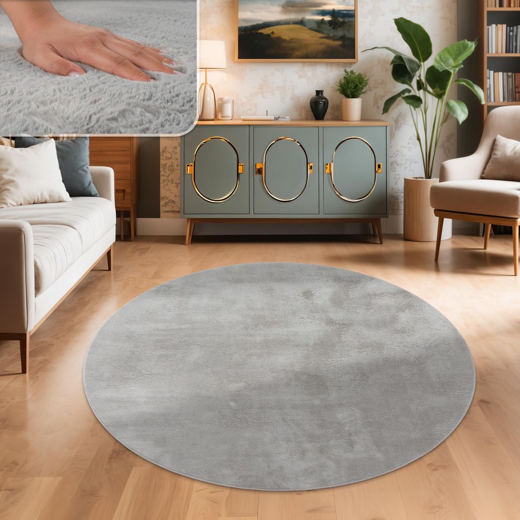 A circular gray rug is placed on a wooden floor in a living room setting, with a sofa, cabinet, and plant visible.