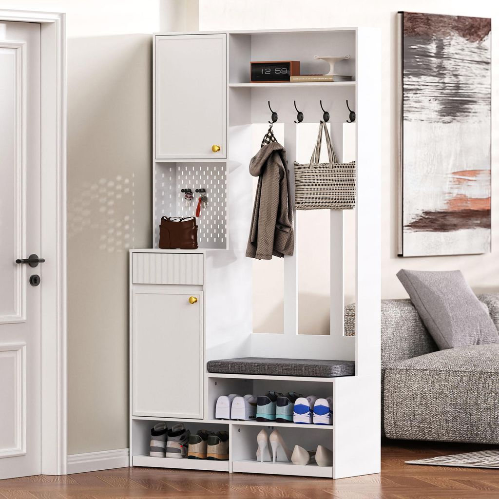 A white entryway storage unit with a bench, hooks, and shelves, placed in a hallway next to a door and a sofa.