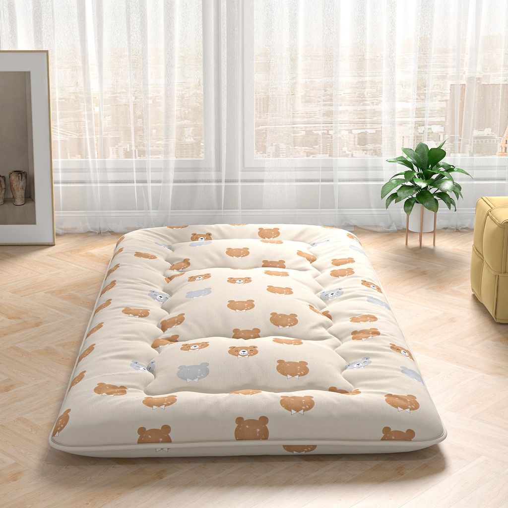 A floor mattress with a bear pattern, placed on a wooden floor in front of sheer curtains.