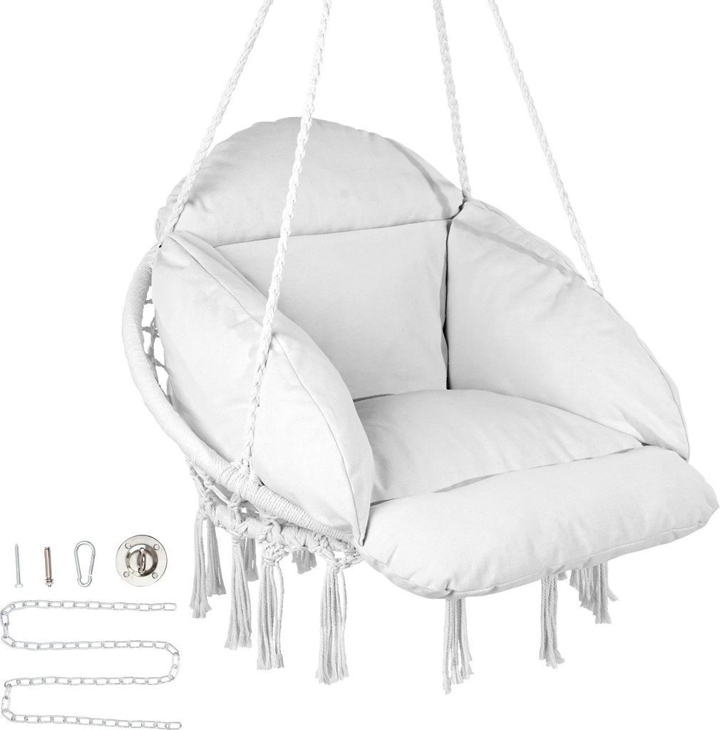 A white macrame hanging chair with cushions and tassels, suspended by ropes. Mounting hardware is visible to the left.
