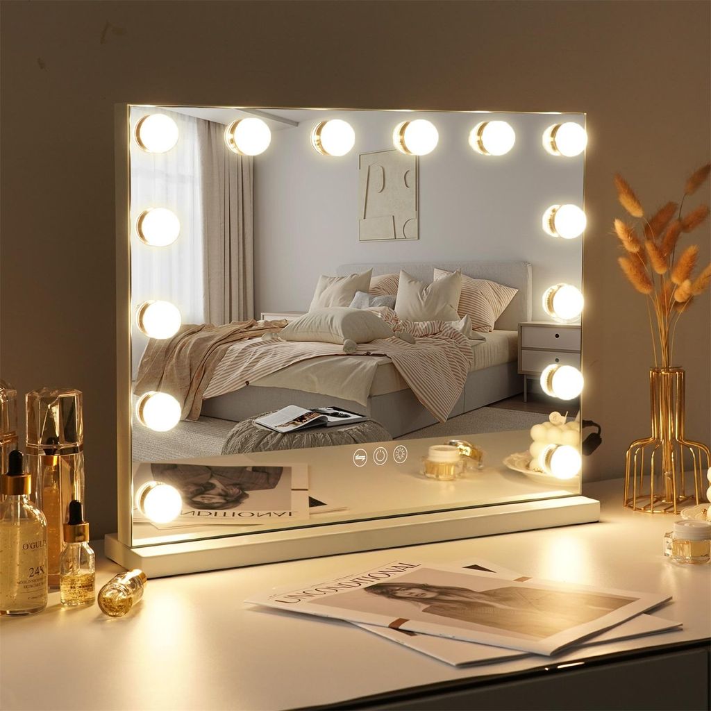 A vanity mirror with lights is placed on a desk in front of a bed.