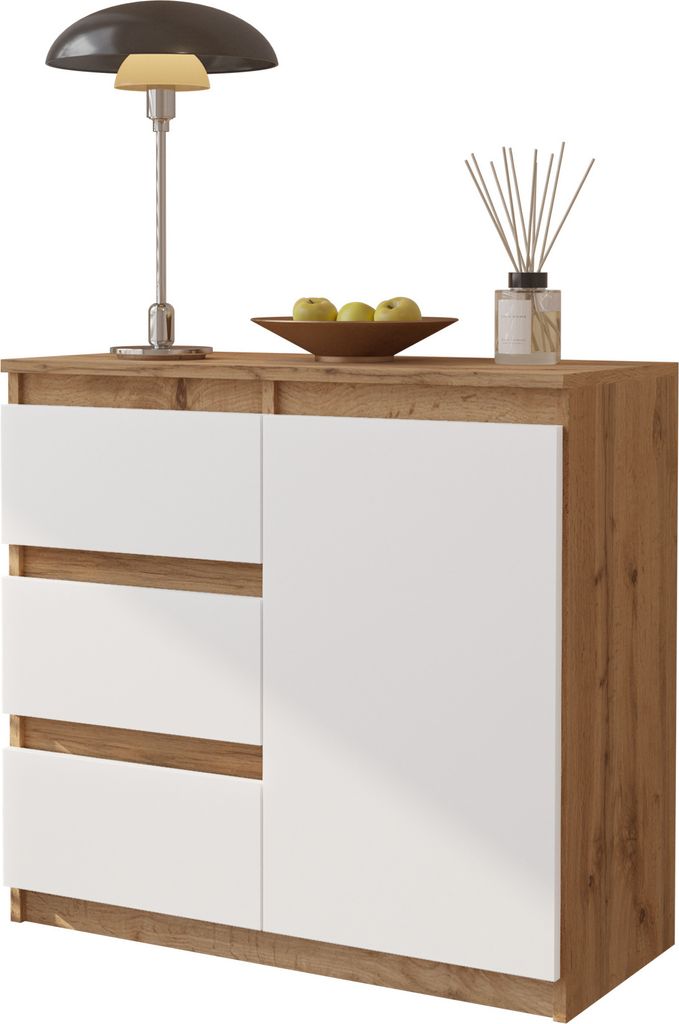 A modern sideboard with white drawers and a wood-grain effect frame, decorated with a lamp, a bowl of apples, and a diffuser.