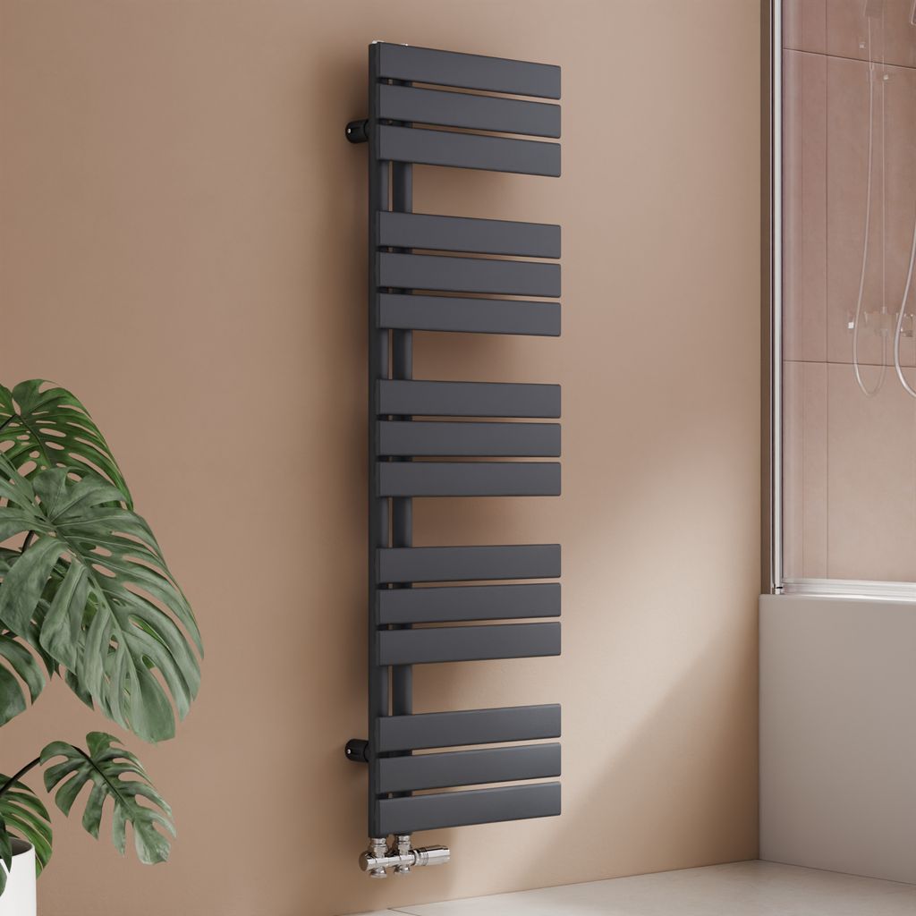 A modern anthracite designer radiator is shown mounted on a light brown wall next to a large green plant. A bathtub and shower screen are visible in the background.