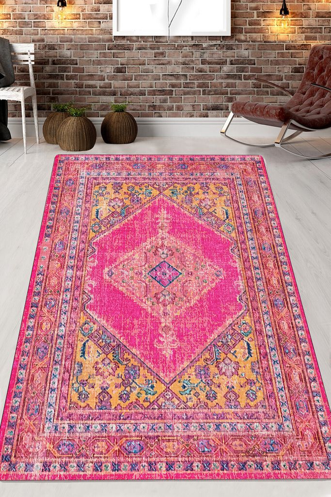 A colorful rug is laid out on a wooden floor in a room with a brick wall and a rocking chair.