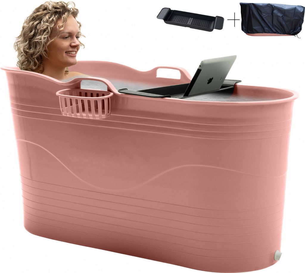 A woman is sitting in a pink portable bathtub, with a laptop and bath tray on top.