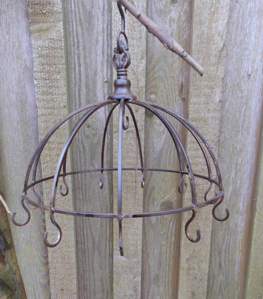 A rustic metal hanging basket with hooks, suspended from a branch against a wooden fence.