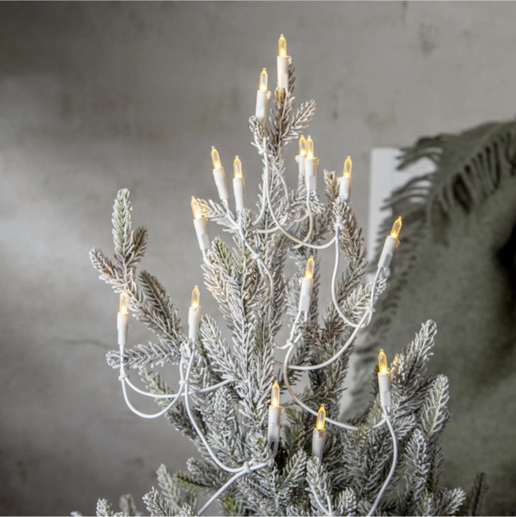 A close-up of a flocked Christmas tree decorated with candle-shaped LED lights.