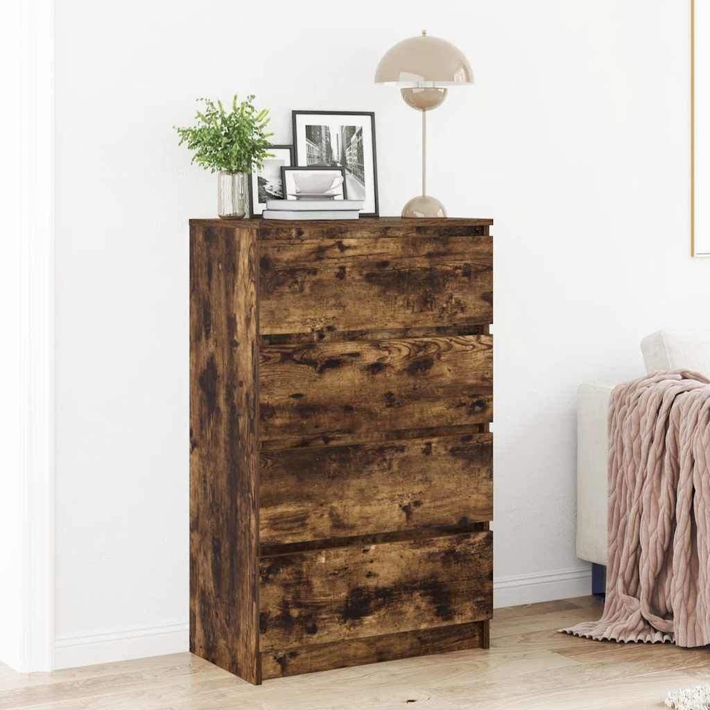 A wooden dresser with four drawers is shown in a room with a white wall and floor. A lamp and some framed pictures are on top of the dresser.