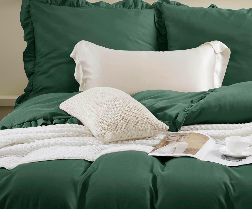A close-up view of a bed with green bedding and white pillows and a blanket.