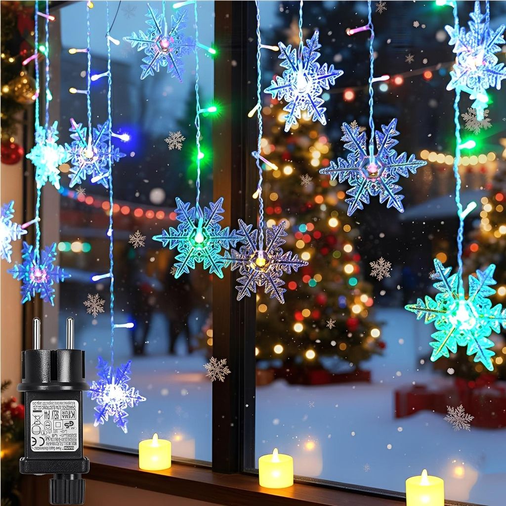 Christmas lights in the shape of snowflakes hanging in a window with a Christmas tree in the background.