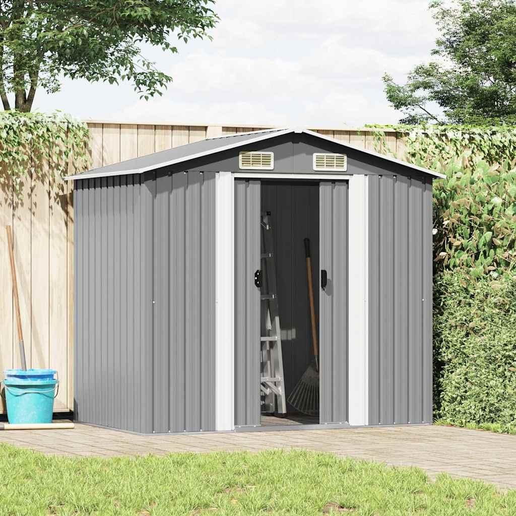 A grey metal garden shed is shown in a backyard setting, with a wooden fence and greenery in the background. Tools like a broom and a ladder are visible inside the open shed.