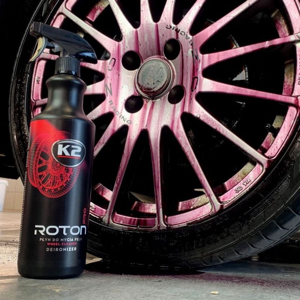 A bottle of K2 Roton Pro wheel cleaner is shown next to a car wheel that has been sprayed with the product, causing it to turn purple.