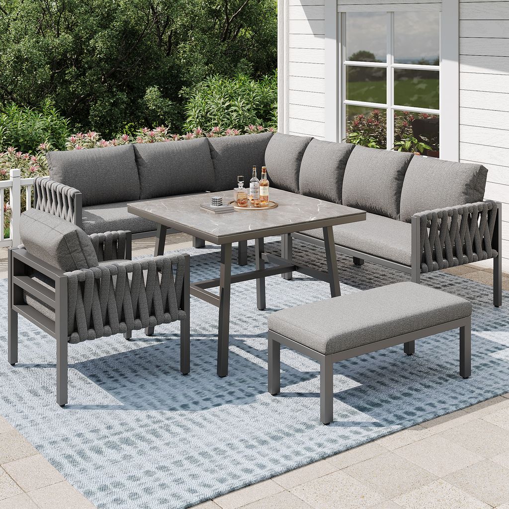 An outdoor patio set with a sectional sofa, table, and bench on a rug.