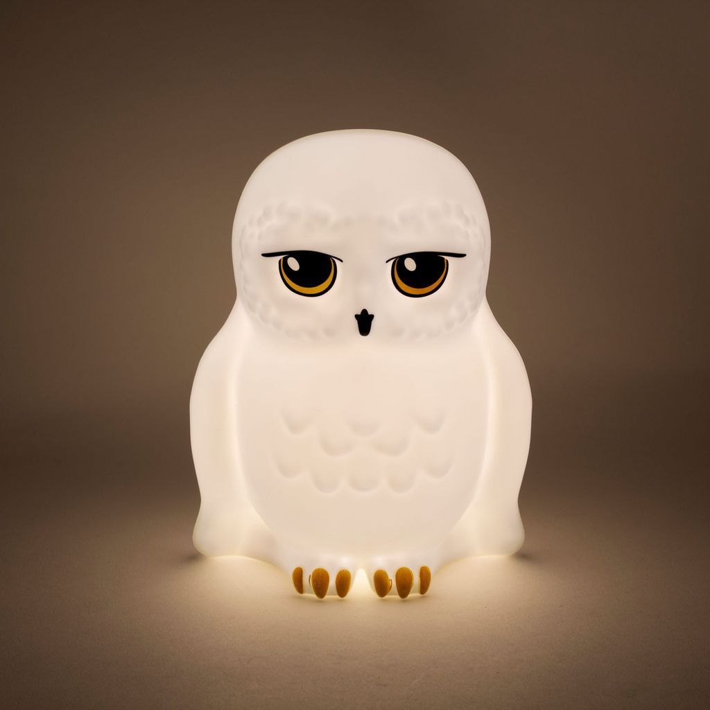 A white owl lamp with yellow eyes and black accents, lit from within, sits on a neutral background.