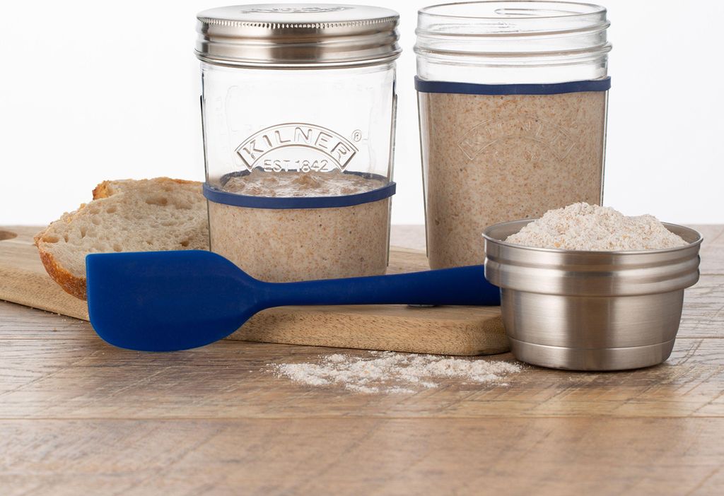 A sourdough starter kit with jars, bread, a spatula, and flour.