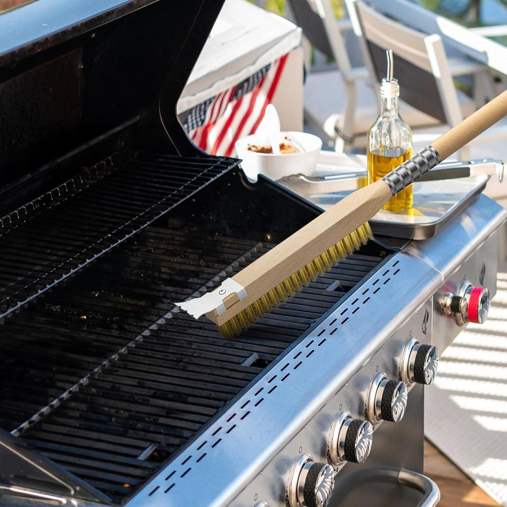 A grill brush is being used to clean a gas grill on an outdoor patio.