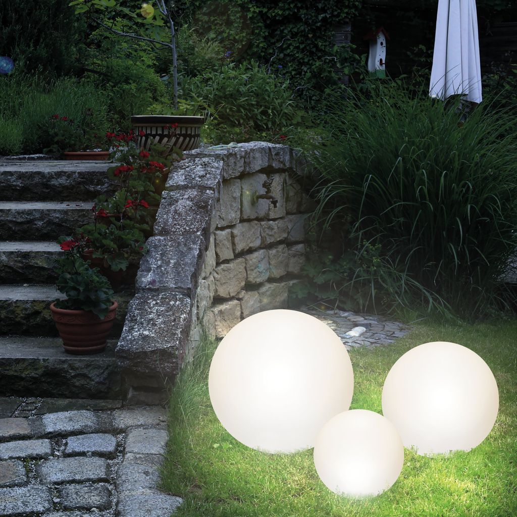 Three illuminated spherical garden lights are placed on a grassy lawn next to a stone pathway and steps.