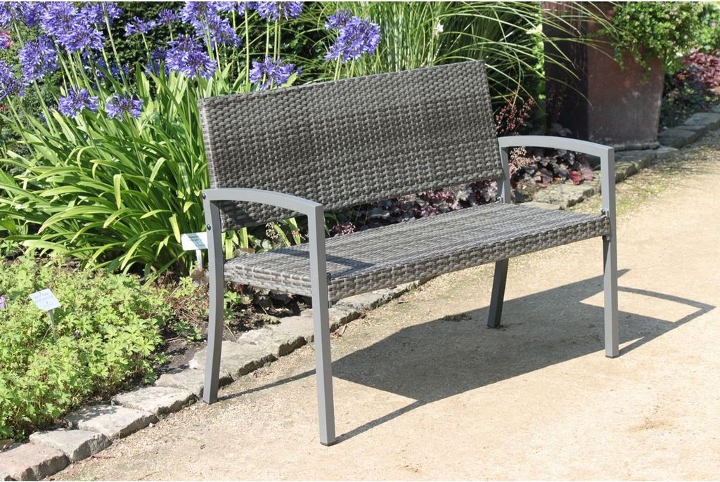 A park bench sits in a garden setting with flowers and plants.