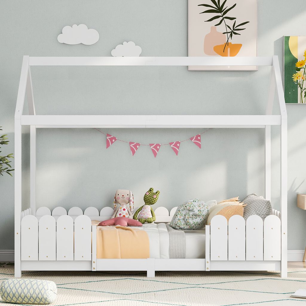 A white house-shaped bed for children, decorated with a pink banner and stuffed animals.