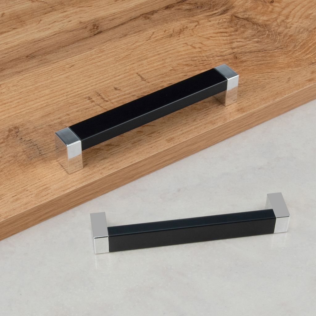 Two black and silver cabinet handles are shown on a wooden surface and a grey surface.