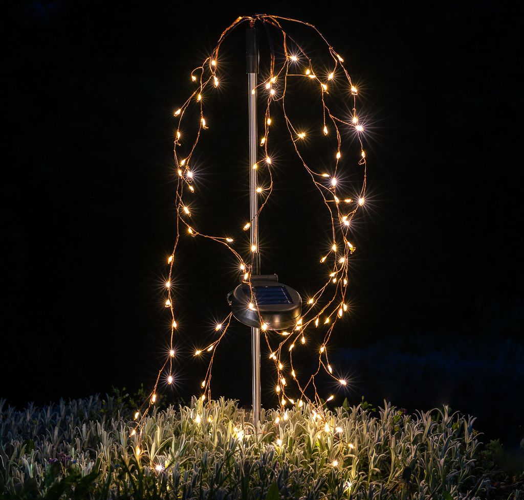 A solar-powered garden light with cascading LED lights at night.